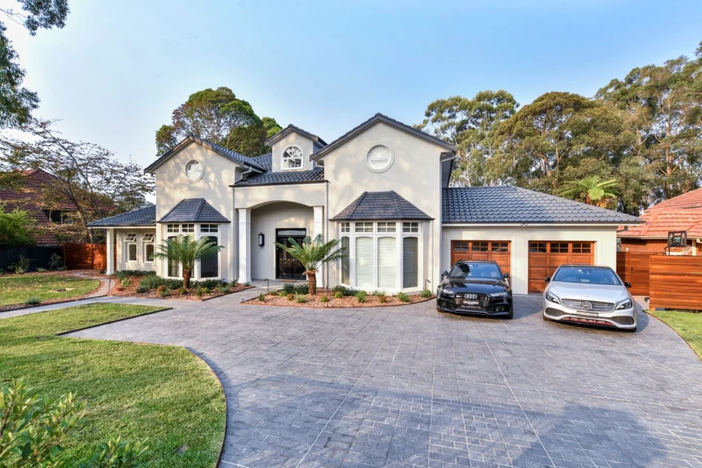 Freshly painted modern two-storey home with landscaped front yard, tiled roof, and luxury cars parked on a paved driveway - Exterior Painting